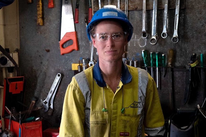 A female in a hard hat with safety glasses and hi vis apparel with tools