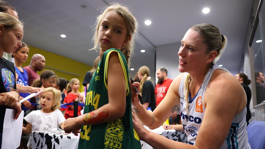 Basketballer Lauren Jackson talks to a young fan as she signs their shirt after an WNBL game.