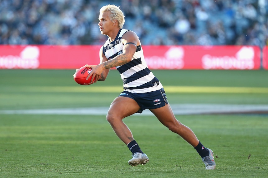 A Geelong AFL player holds the ball in two hands as he prepares to kick.