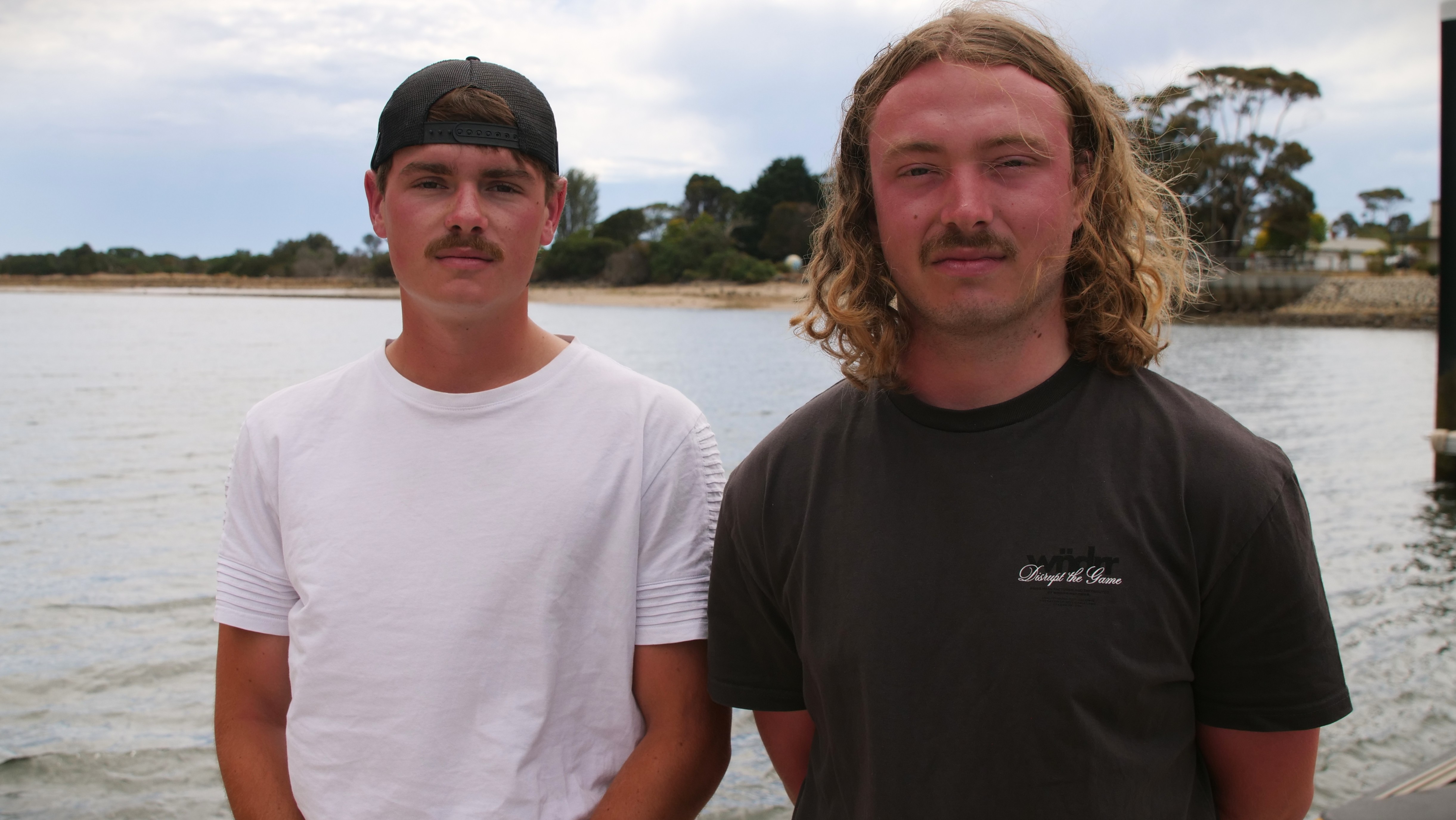 Dois jovens olham para a câmera, numa praia