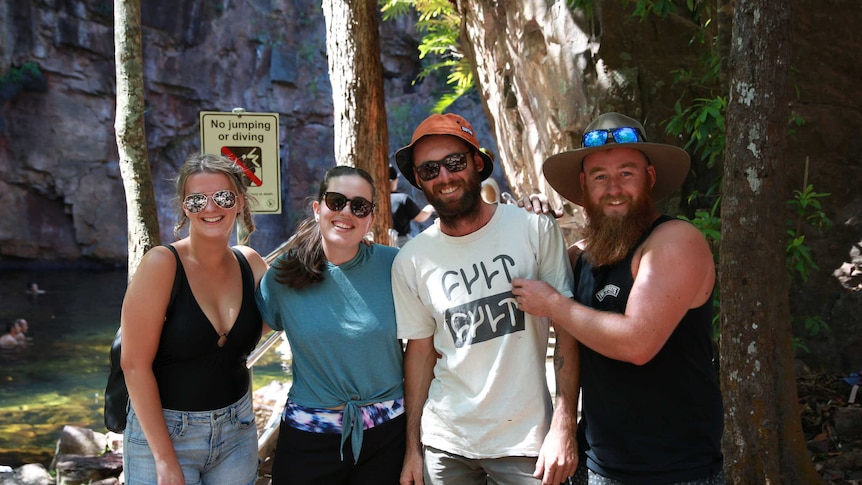 Four smiling people pose for the camera in front of a waterfall