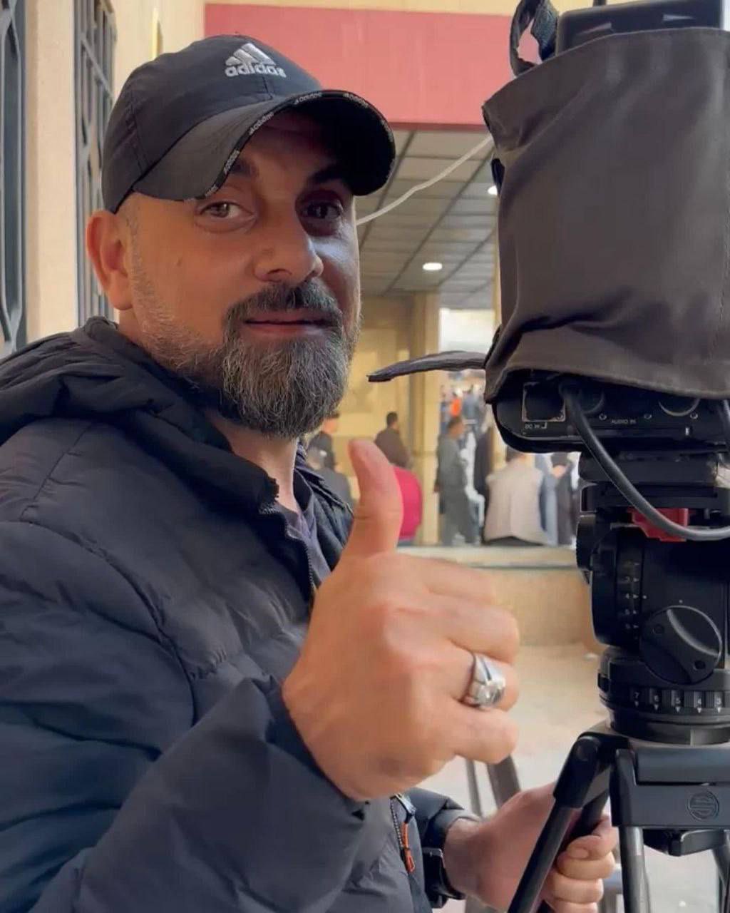 Samer Abu Daqqa behind a camera giving a thumbs up. 