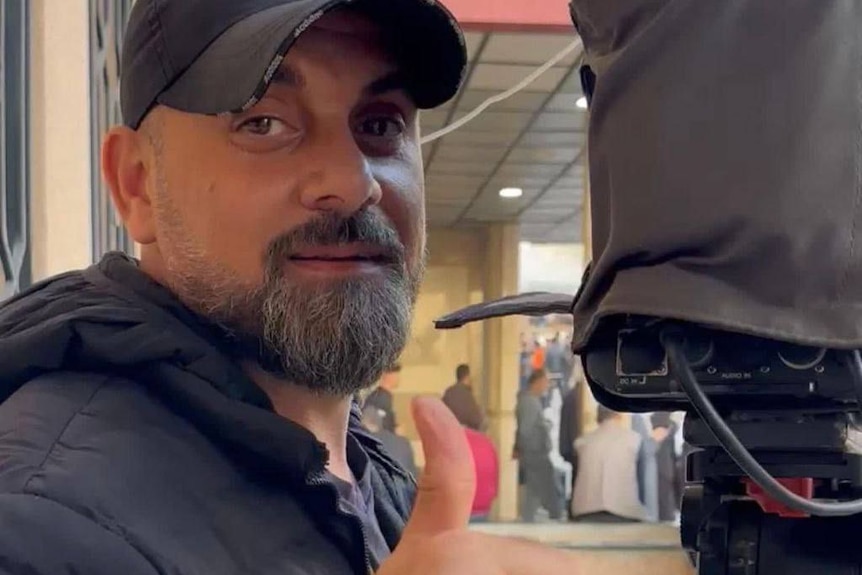 Samer Abu Daqqa behind a camera giving a thumbs up. 