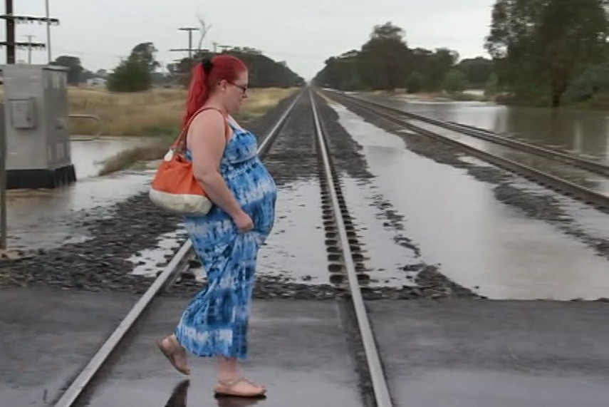 A pregnant woman walks across train tracks with floodwaters in the background.