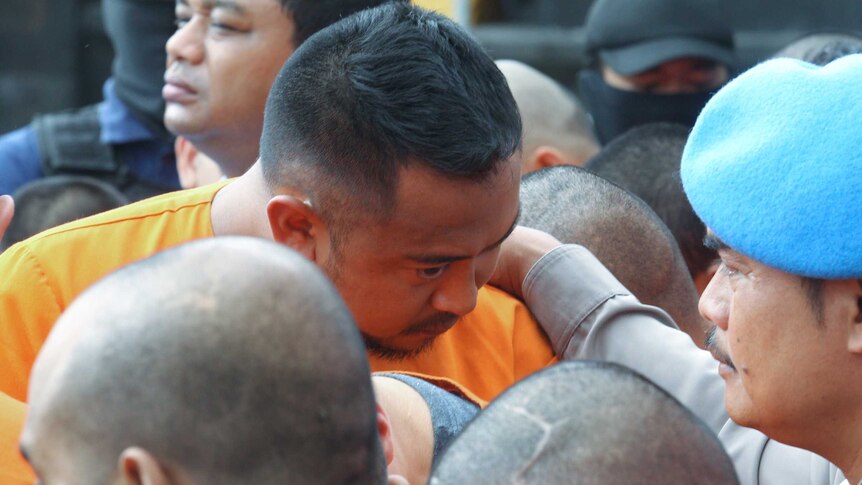 William Cabantog, in an orange prison jumpsuit, has his head down as Indonesian police lead him around outside.