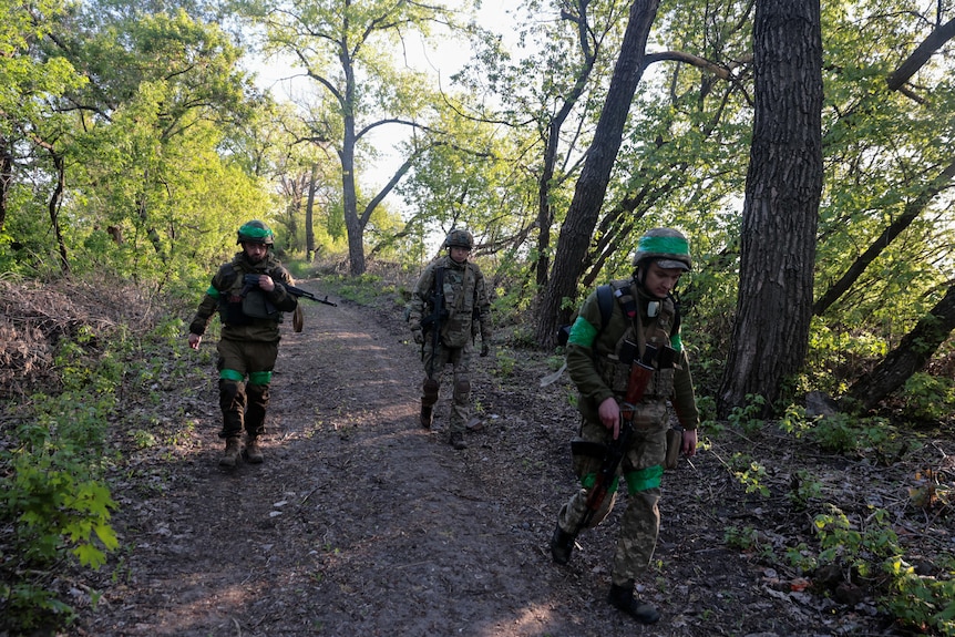 Three Ukrainian soldiers in camouflage walk down a forest path.