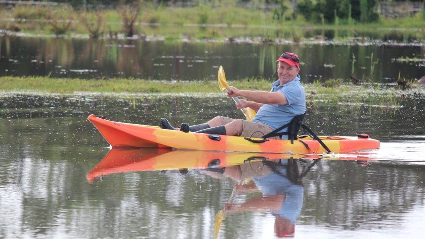 Farmer in a kayak paddling across a flooded paddock.