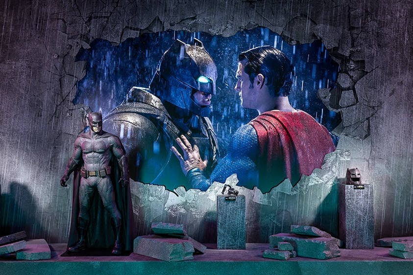 A stage display featuring a bulky costume in front of a bright poster of Batman and Superman