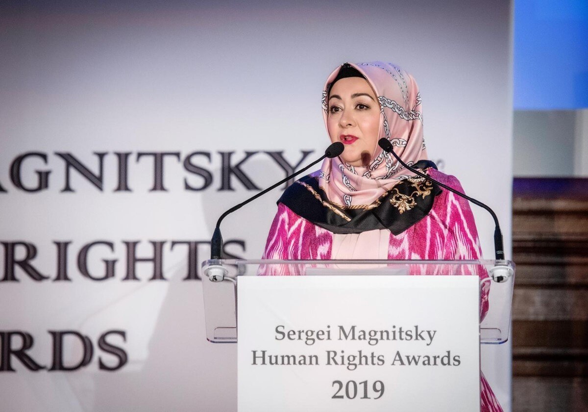 A woman speaks into a microphone at a podium on a stage.