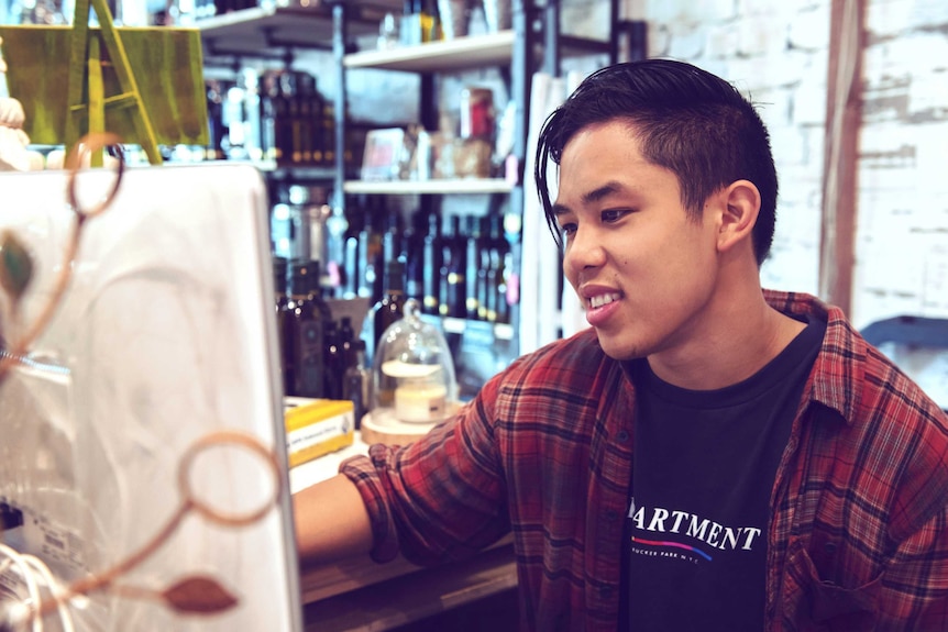 A man sits behind the counter of a retail shop, workers may need to keep working during redundancy consultation.