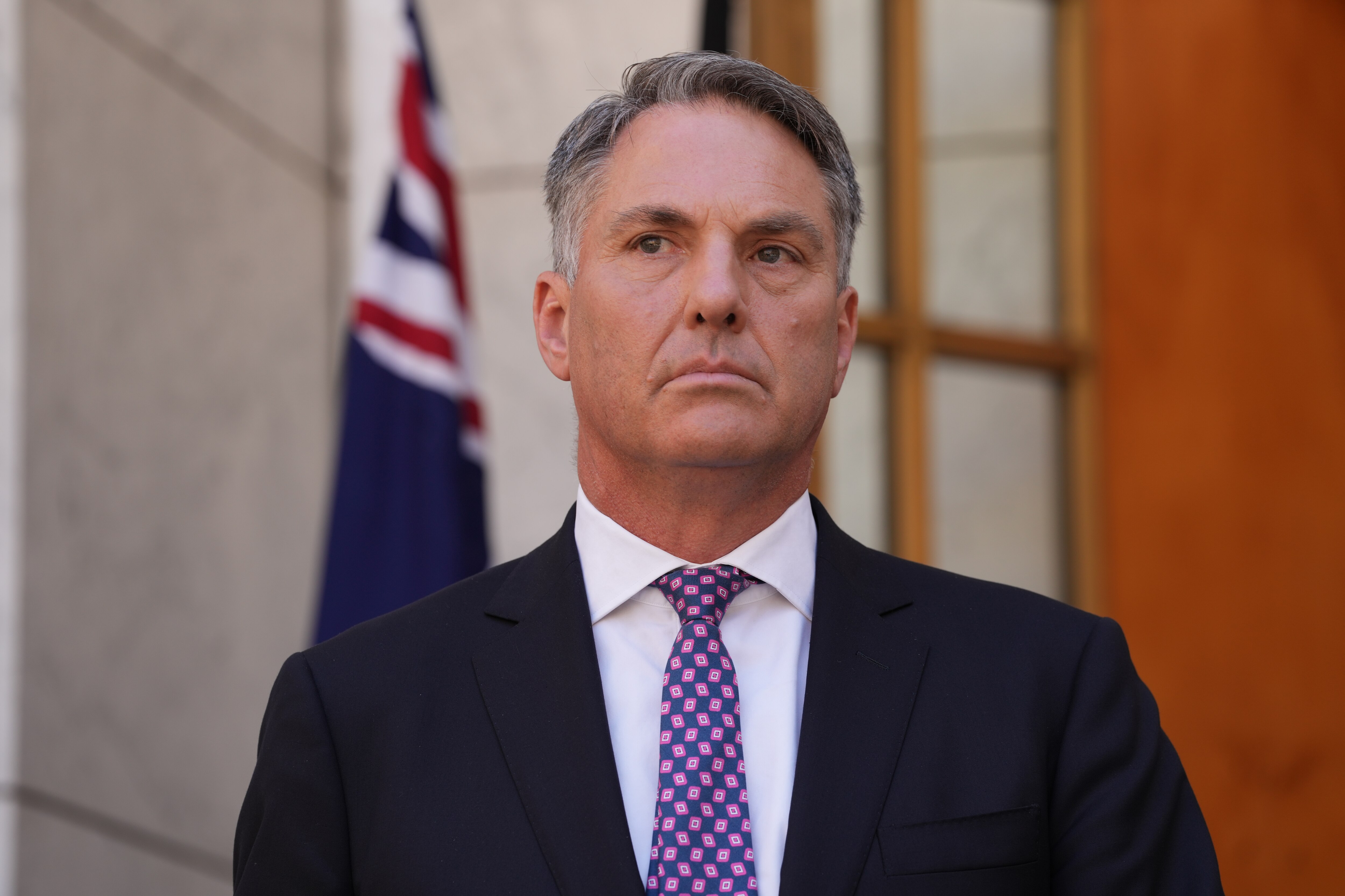 Man listening to reporters' question, Australian flag behind him