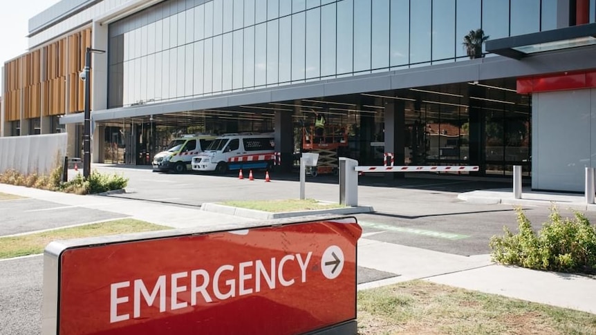 A picture of an emergency sign, with carpark, ambulances and windows in background, outside a hospital's Emergency Department 