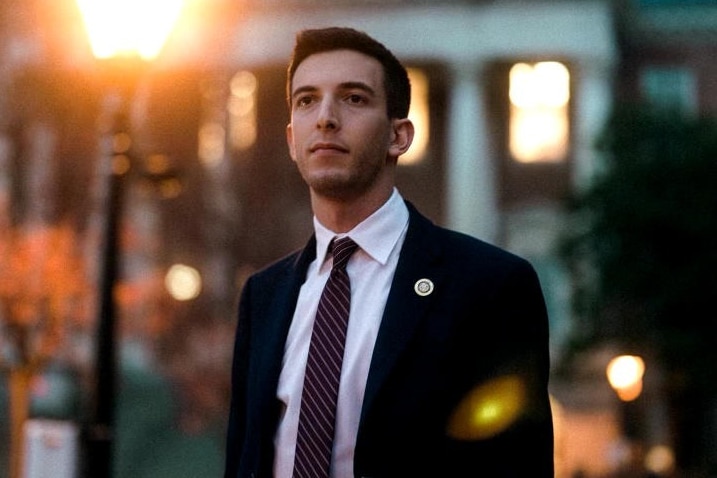 A man stands outside at dusk wearing a suit. 