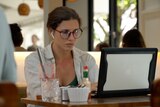 A young woman in airpods looks at a laptop screen in a cafe 
