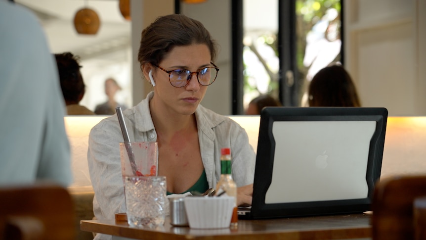 A young woman in airpods looks at a laptop screen in a cafe 