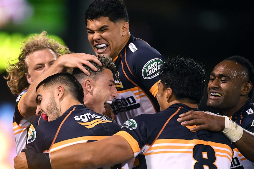 The Brumbies Super Rugby AU players embrace as they celebrate a try against the Queensland Reds.