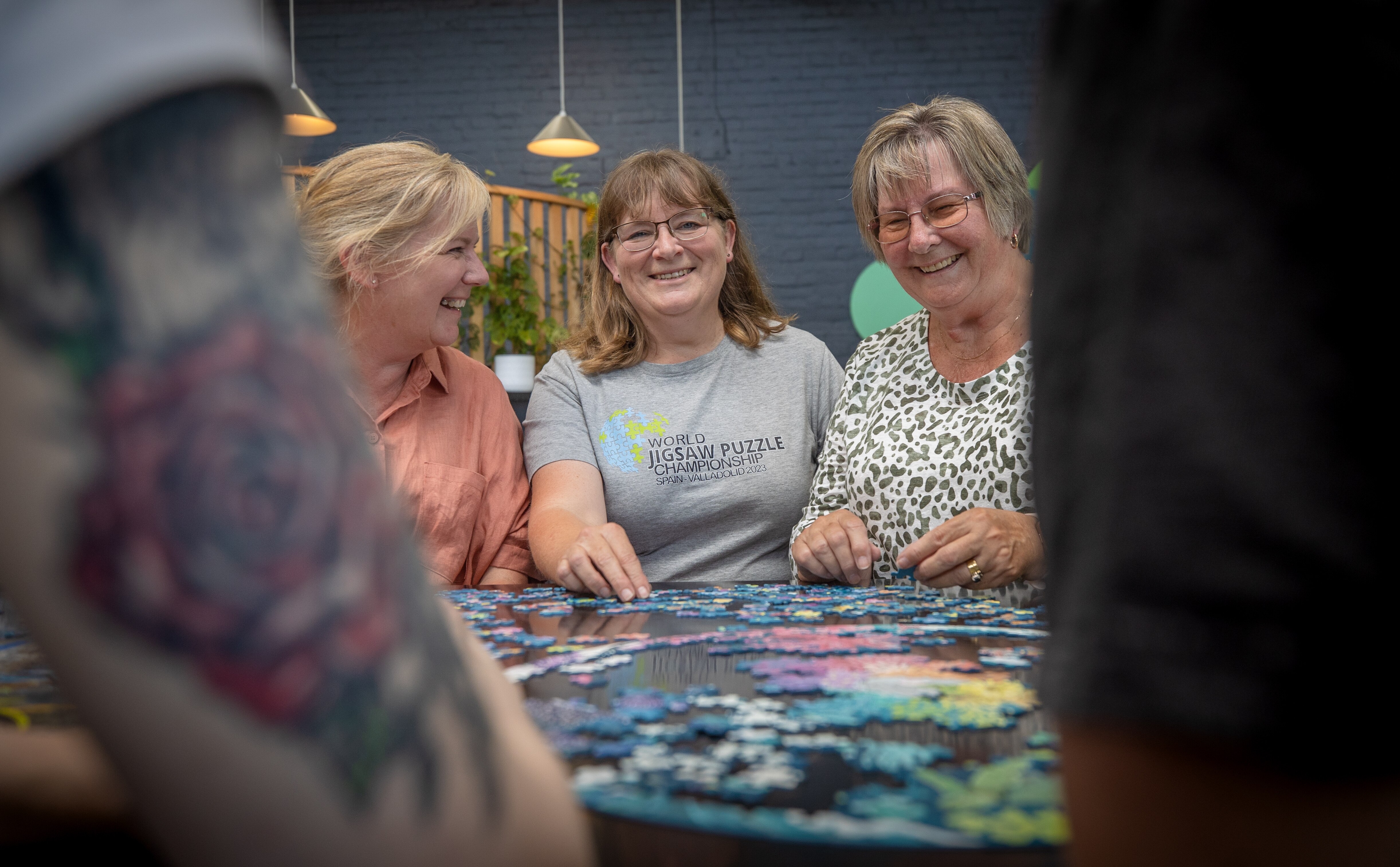 A photo taken from above of four people doing a jigsaw puzzle together on a black table