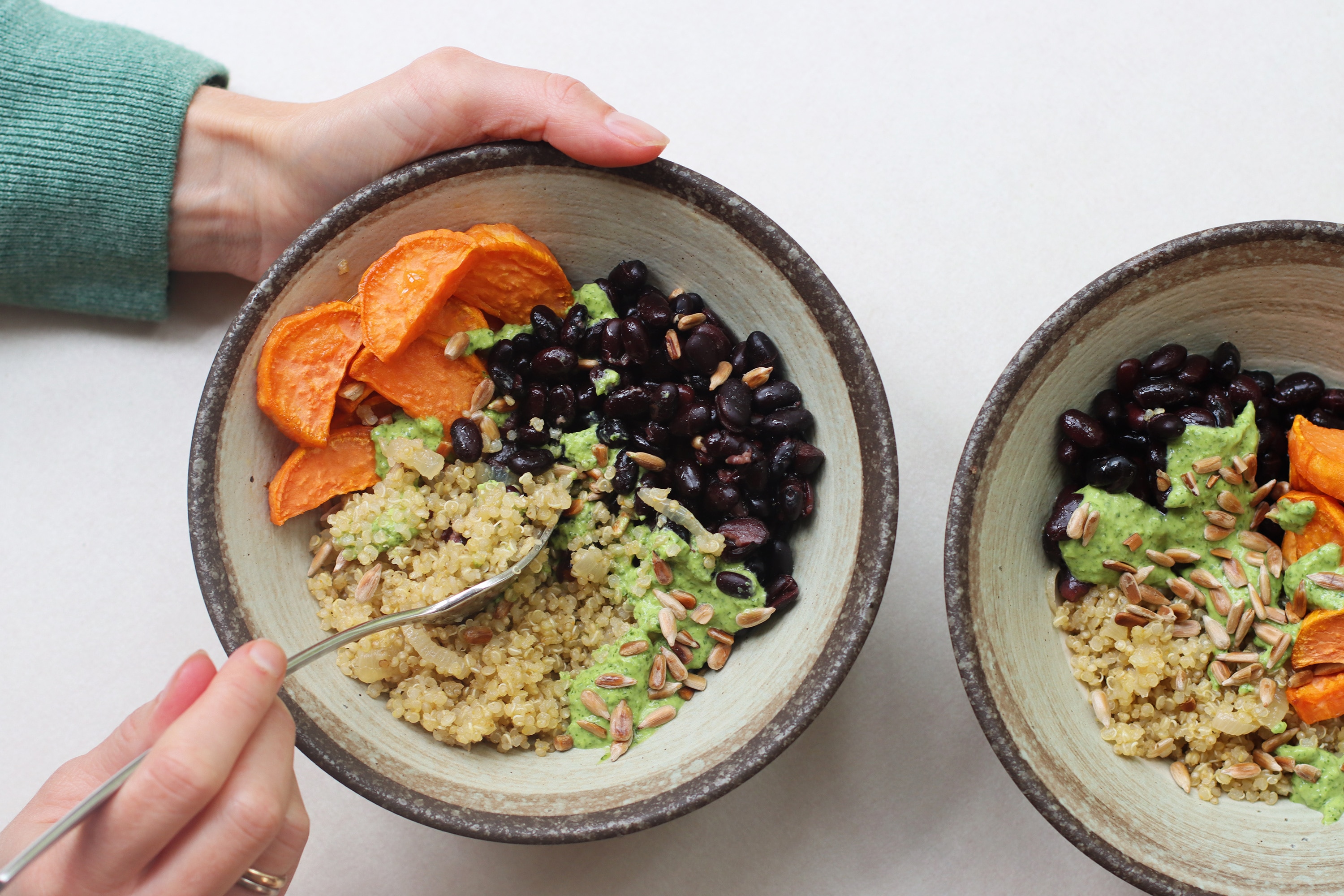 Hands holding a bowl with quinoa, roasted sweet potato, black beans and sunflower seeds.