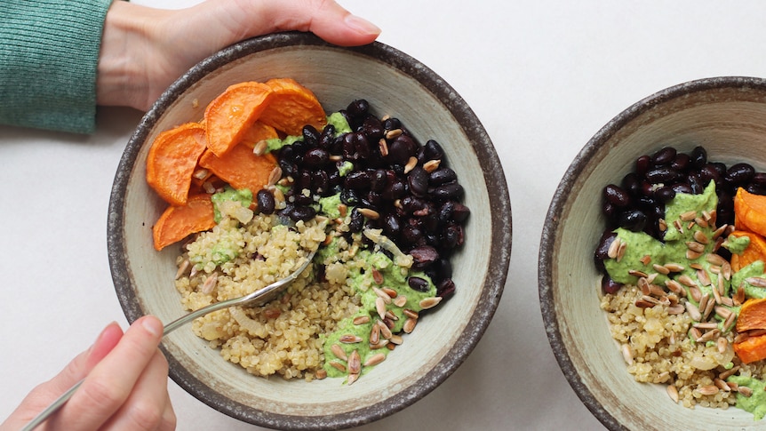Hands holding a bowl with quinoa, roasted sweet potato, black beans and sunflower seeds.