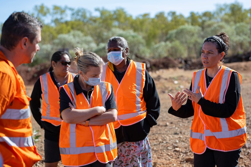 A group of people stand negotiating in high-vis vests.