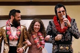 a man and a woman with leis around their necks are walked down the aisle of a chapel by an Elvis Presley impersonator 