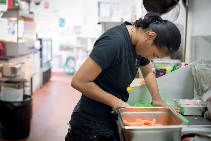 Vaikura Maurangi cuts vegetables in the cafe kitchen.