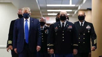 Donald Trump wearing a face mask walking next to military generals.