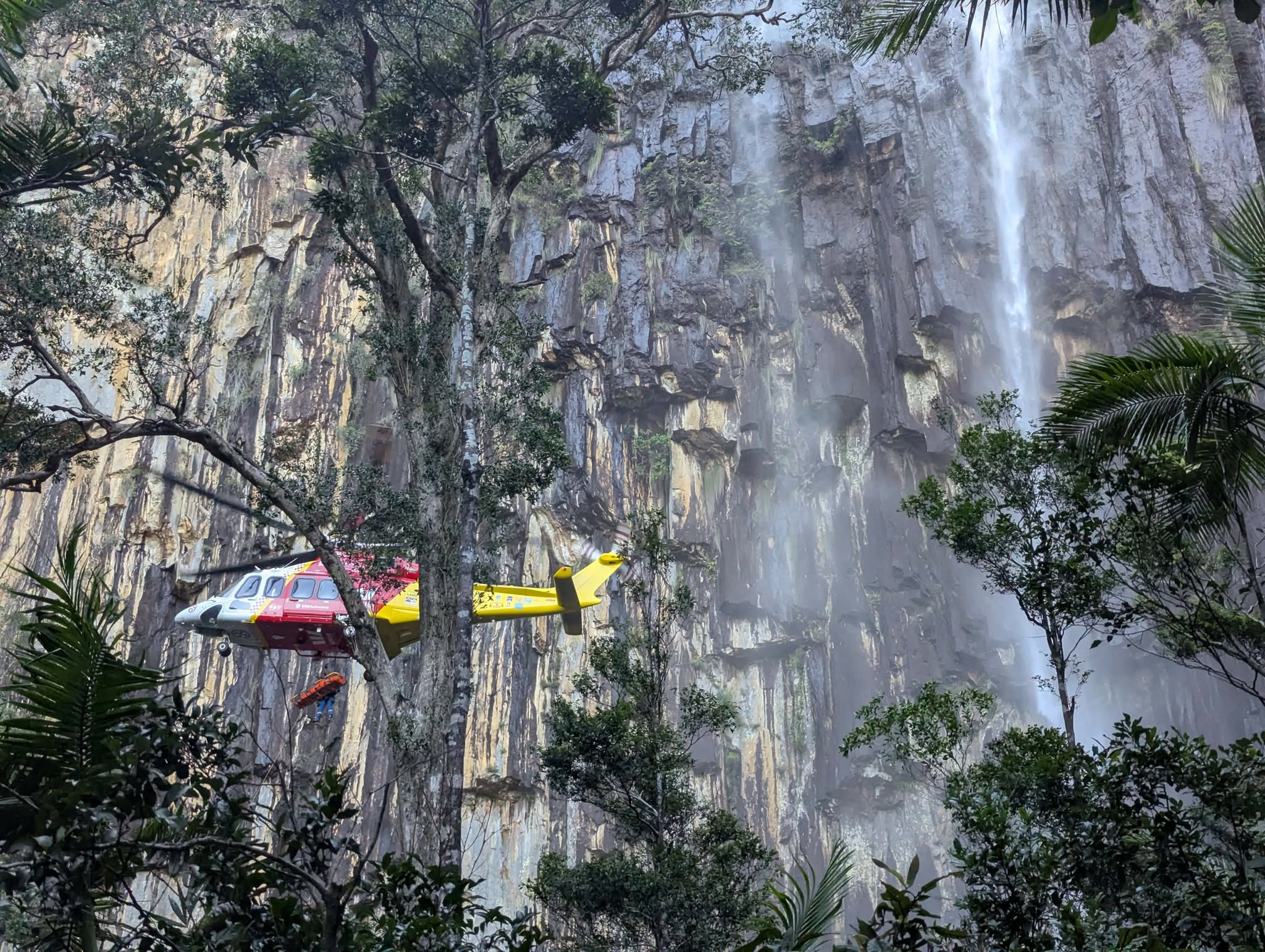 a westpac rescue helicopter hovering in front of a waterfall 