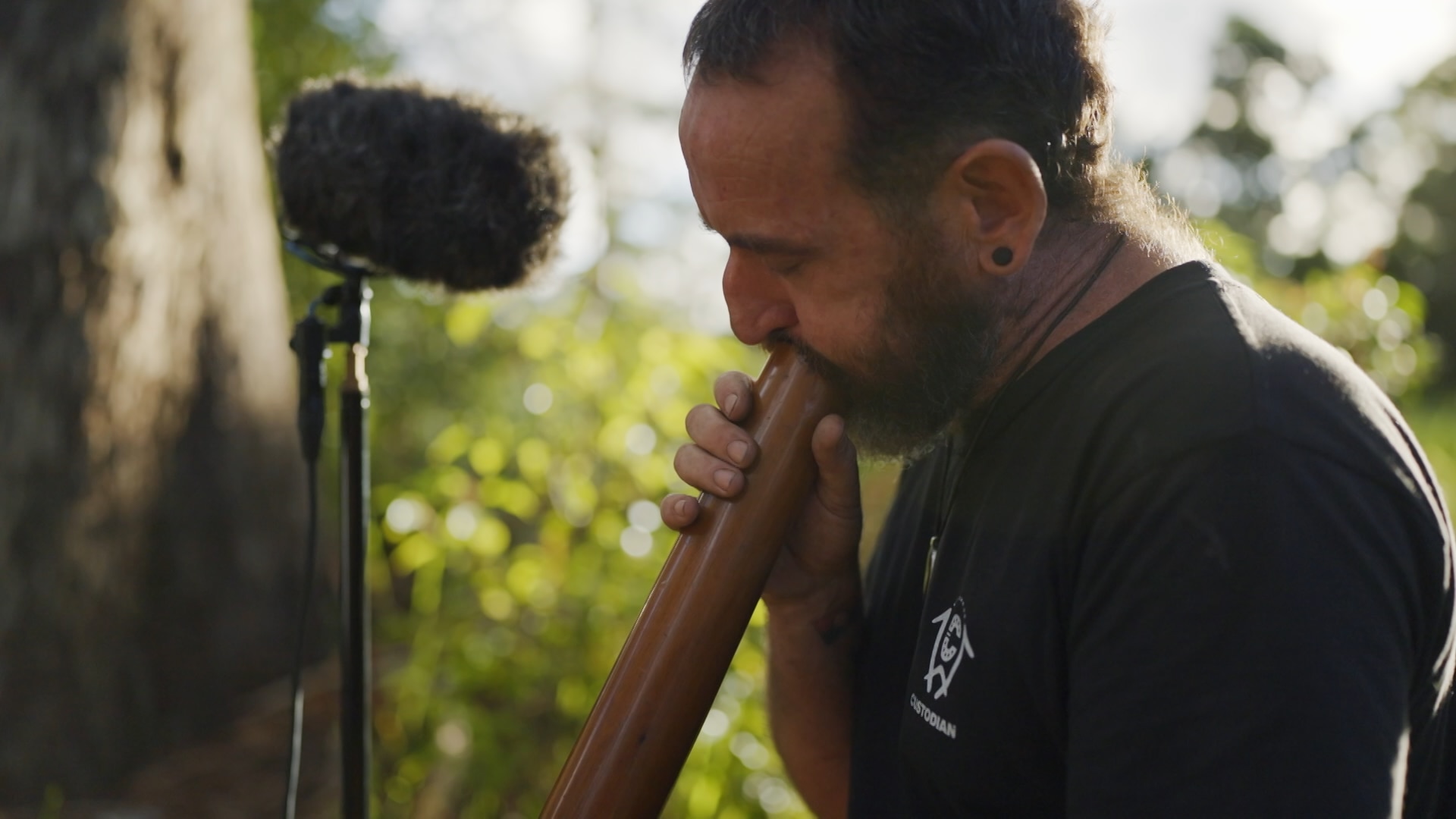 Man playing a didgeridoo as microphone records him.