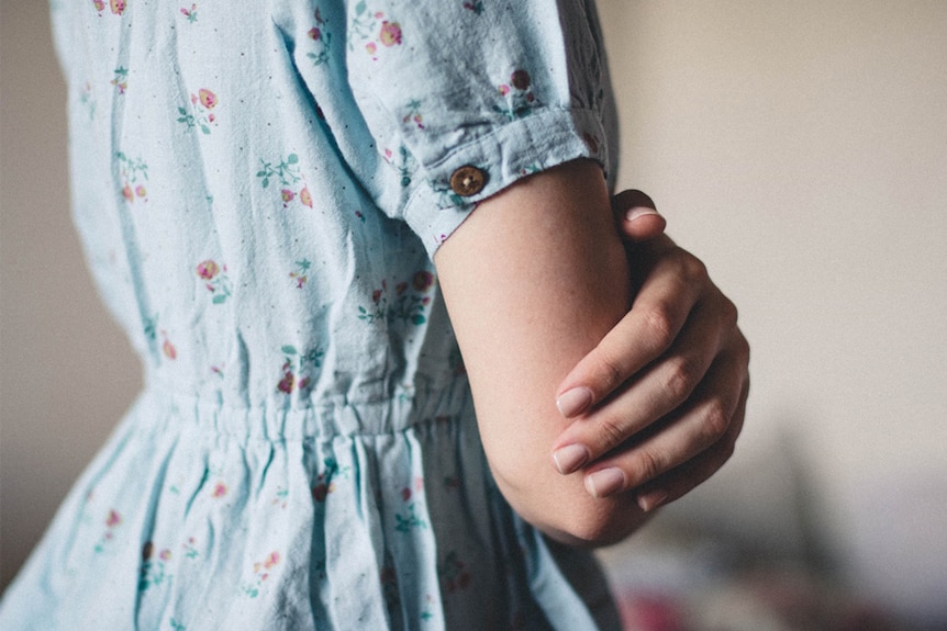 A woman in a floral dress with folded arms.