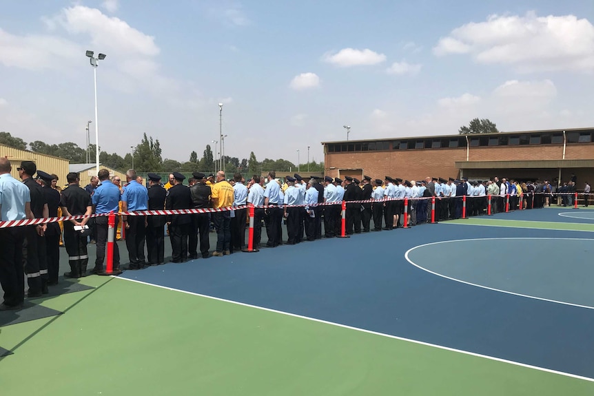 Dozens of RFS career firefighters, volunteer firefighters and basketball players stand to form a guard of honour,.