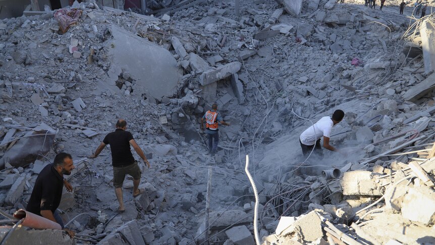 Several people are climbing on bits of rubble, searching for people underneath the rubble.