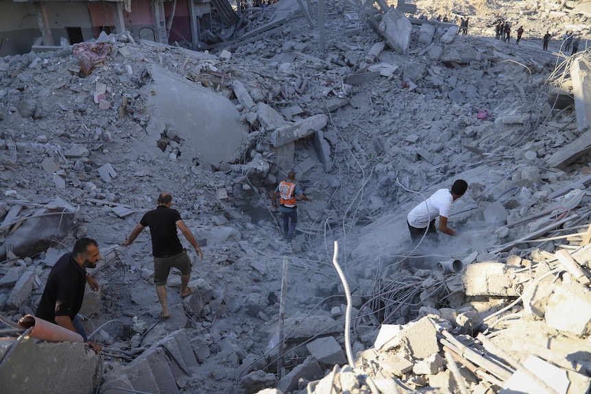 Several people are climbing on bits of rubble, searching for people underneath the rubble.