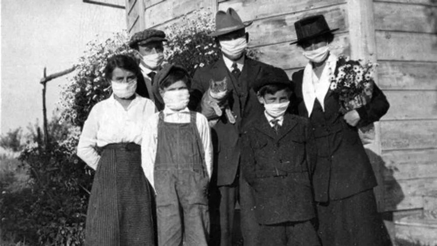 Black and white photograph of a family, all wearing masks, with the father holding the family cat