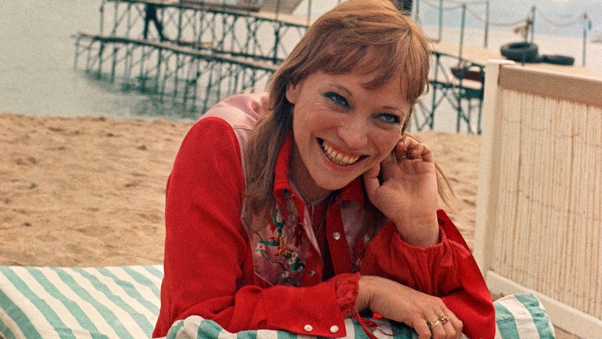 Anna Karina rests on a chair smiling at a beach in Cannes