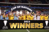 A soccer team wearing yellow and green lifts a trophy after winning a friendly tournament
