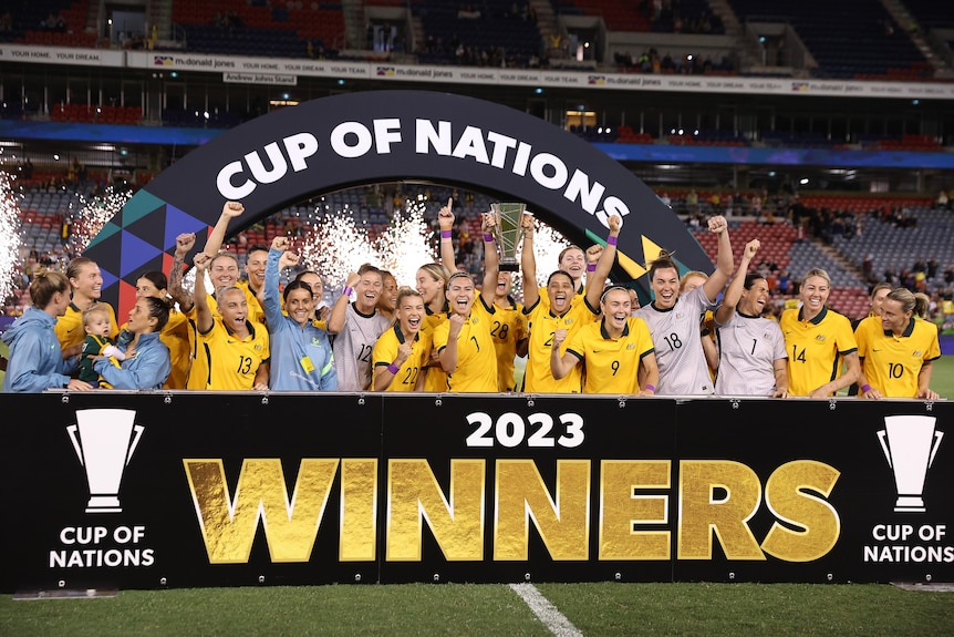 A soccer team wearing yellow and green lifts a trophy after winning a friendly tournament