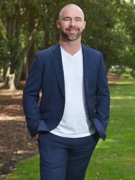 Man in navy jacket and white-T-shirt standing a park