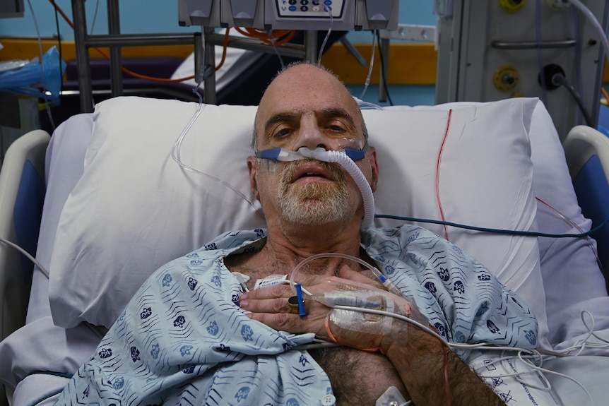 A man looks at the camera from his hospital bed.