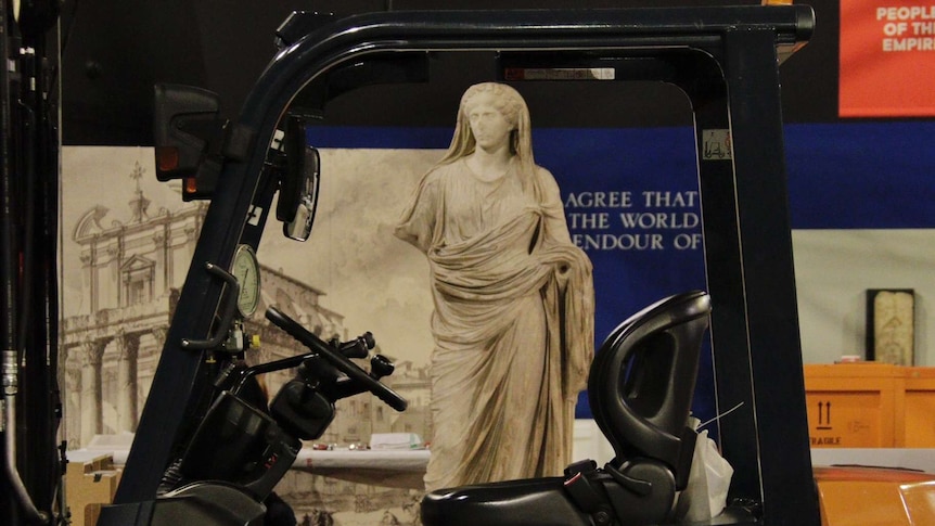 A forklift sits in front of a statue in a museum.