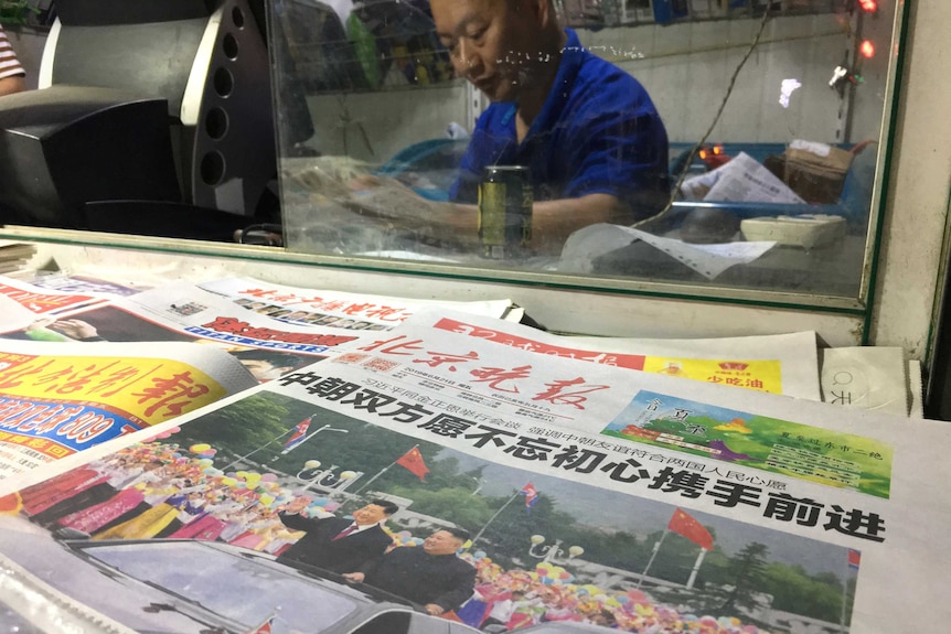 The front page of a Chinese newspaper shows Chinese President Xi Jinping on a newspaper stand while a man works behind.