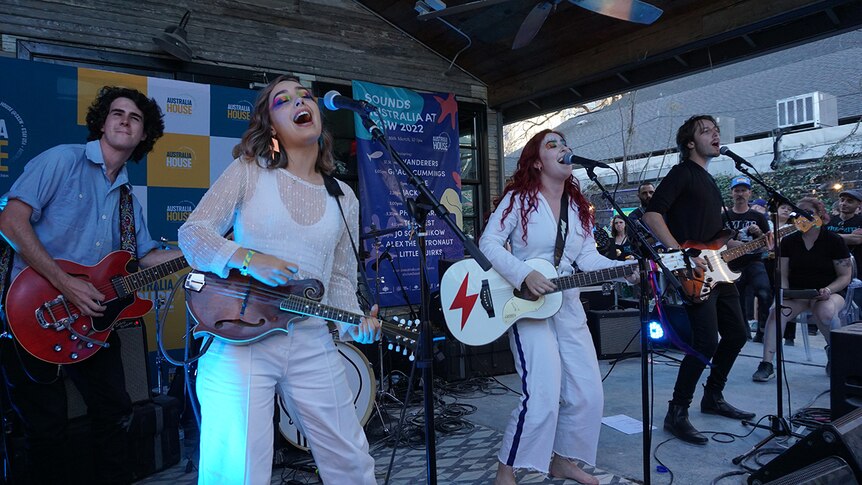 Two women and two men perform on stage at Austin's SXSW festival. The women have colourful eye make up and wear white
