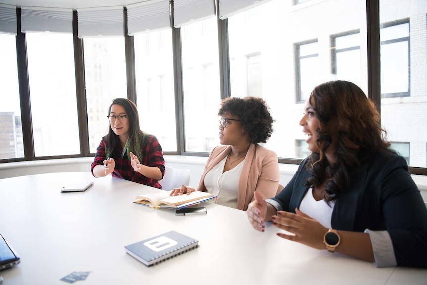 Three women in an office meeting to depict a story about the use of gendered terms like "hey guys".