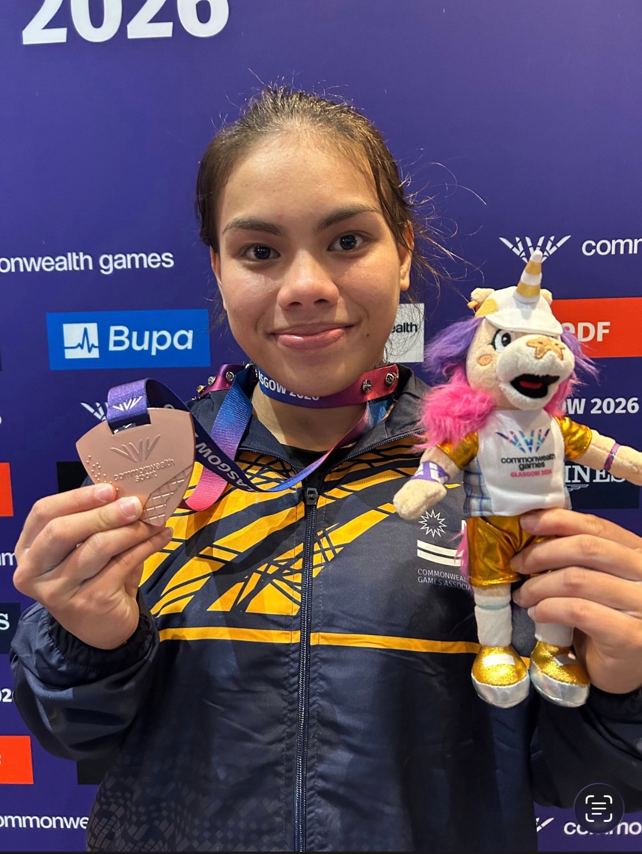 A young woman from Nauru wearing an athletics uniform and holding a Commonwealth Games toy and a bronze medal.