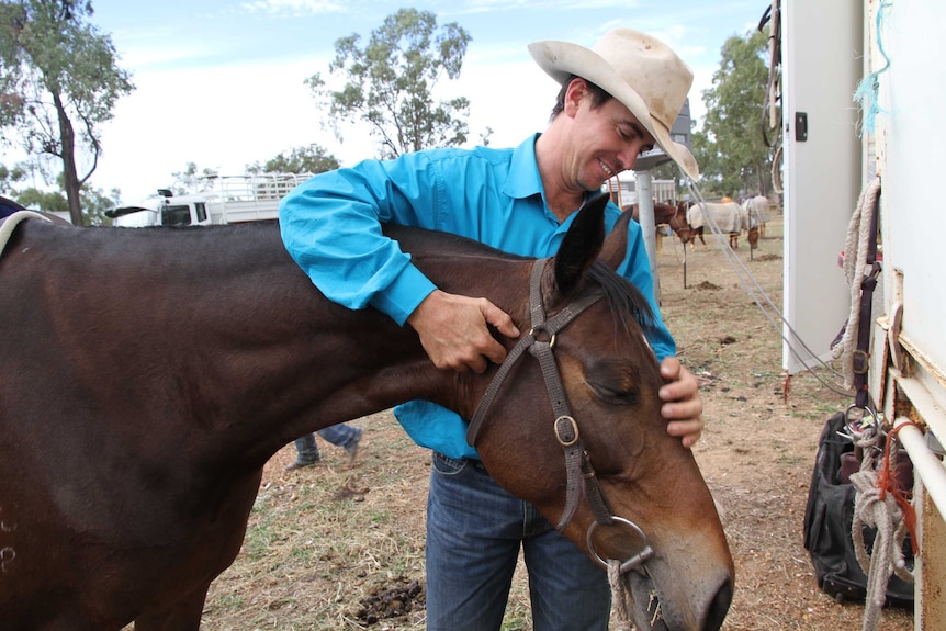 A man in a bright blue shirt and jeans patting his campdrafting horse 