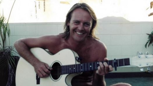 Colour photo of Crispin Dye smiling and playing a guitar in an undated photo
