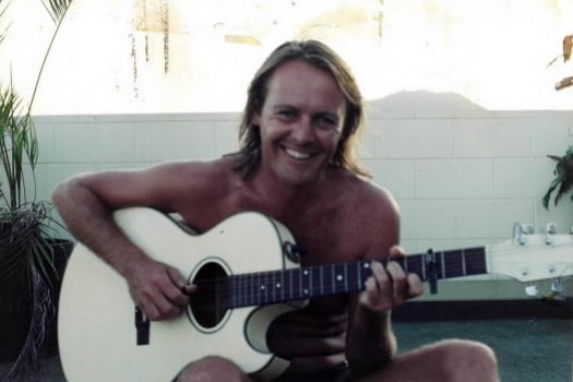 Colour photo of Crispin Dye smiling and playing a guitar in an undated photo