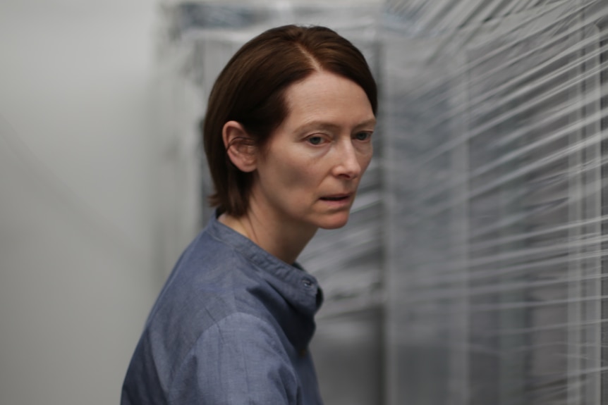 Middle-aged woman with short, combed dark hair, wearing a dull blue shirt presses fingers into plastic wrapping on storage units