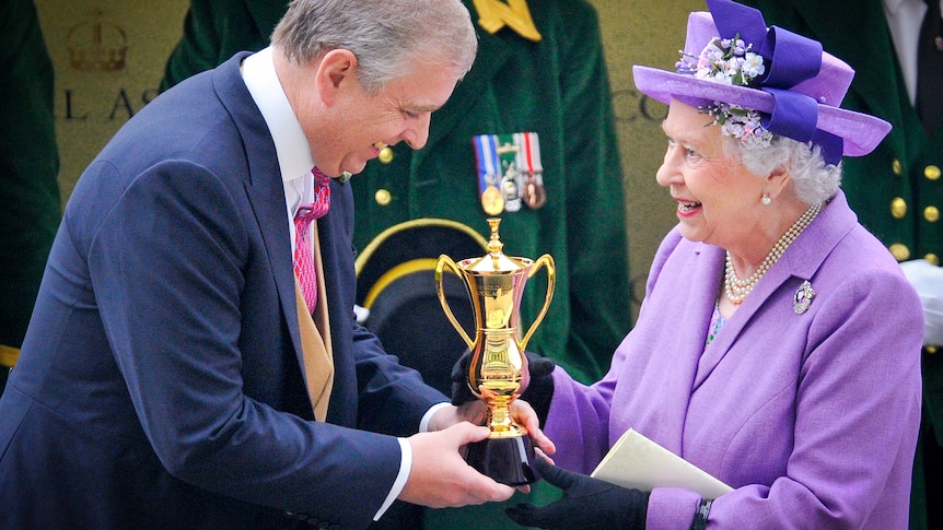 The Queen in a purple outfit smiles while receiving a gold trophy from her son, Prince Andrew