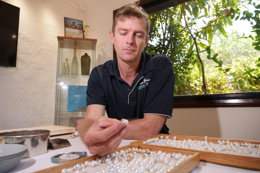 A man holding a pearl up over a tray of pearls inside a room